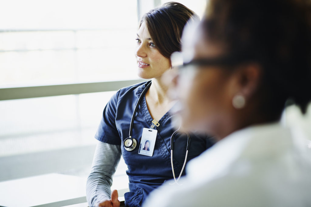 Female nurse listening during medical team meeting with colleagues in hospital