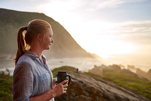 A women looks out at nature while holding a travel mug.