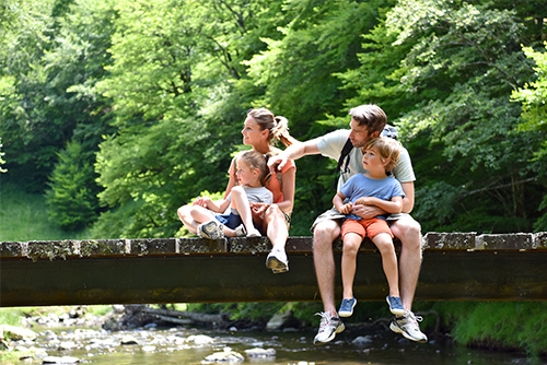 A family sits on a bridge over a creek and looks off to the left.