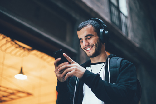 A man is wearing headphones and smiling at his phone.