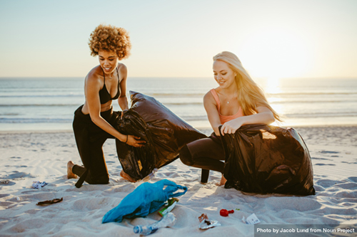 Two women clean up trash on the beach.