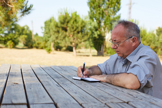 Older man writing his diary in the park on a sunny day