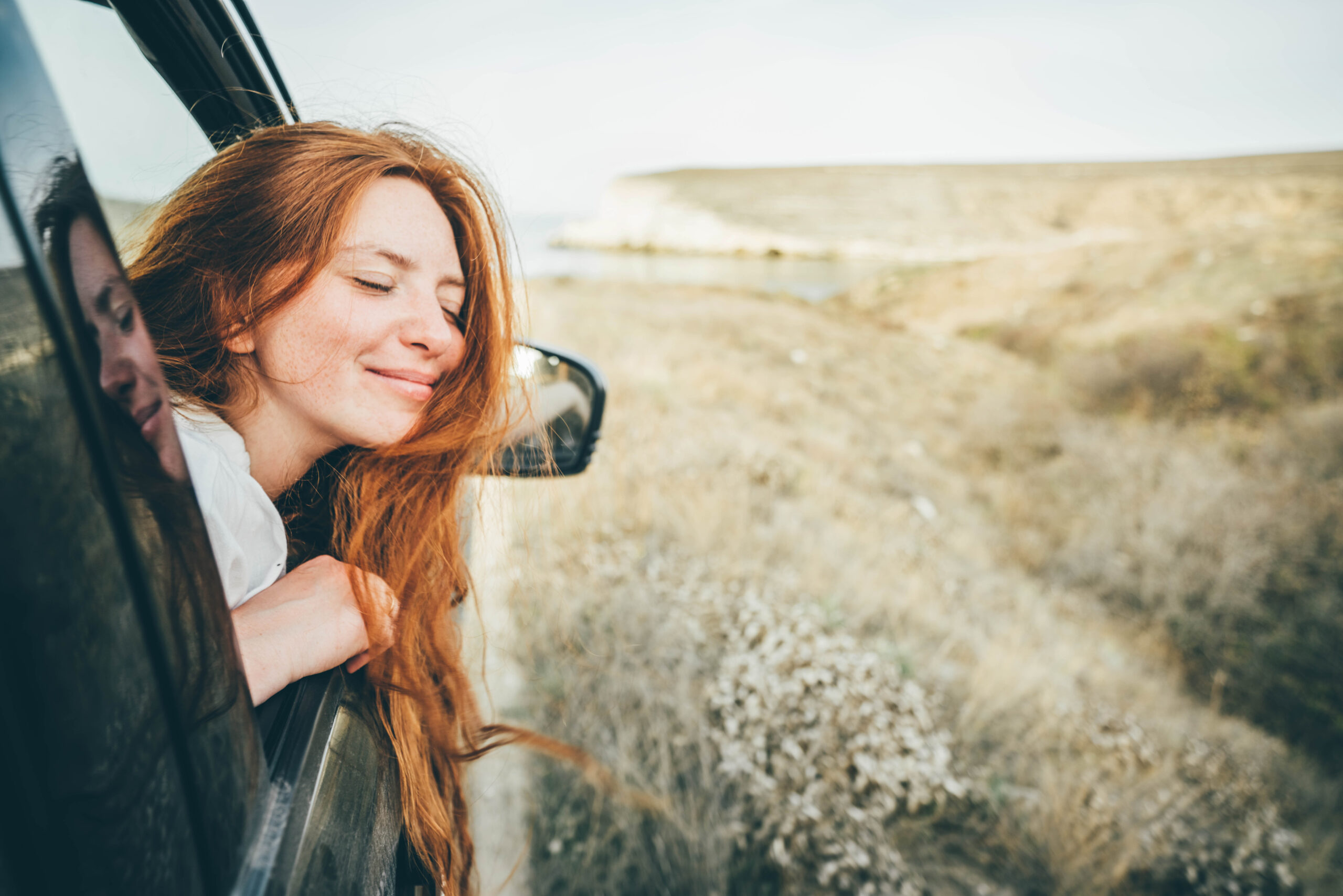 Happy young woman looking out of car window.