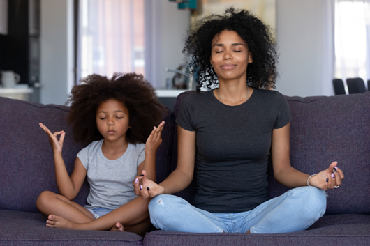 African American woman and her daughter on a couch, in a meditative pose