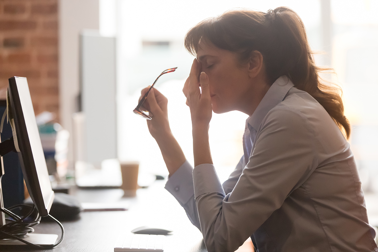 Exhausted female worker sit at office desk take off glasses feel unwell having dizziness or blurry vision, tired woman employee suffer from migraine or headache unable to work. Health problem concept