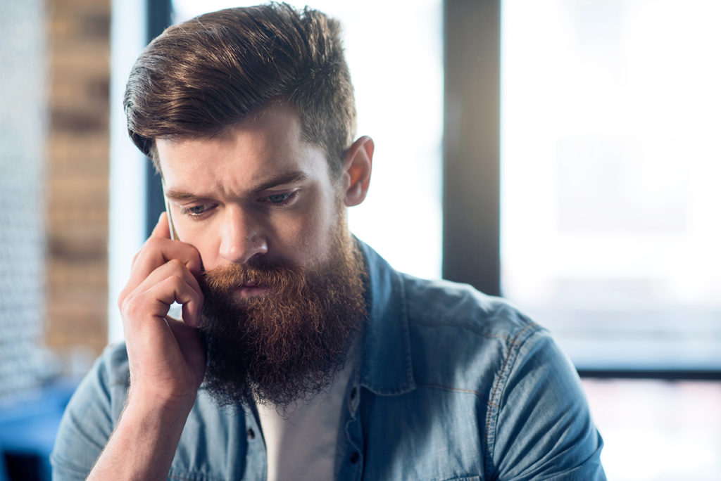 Pleasant bearded man using cell phone