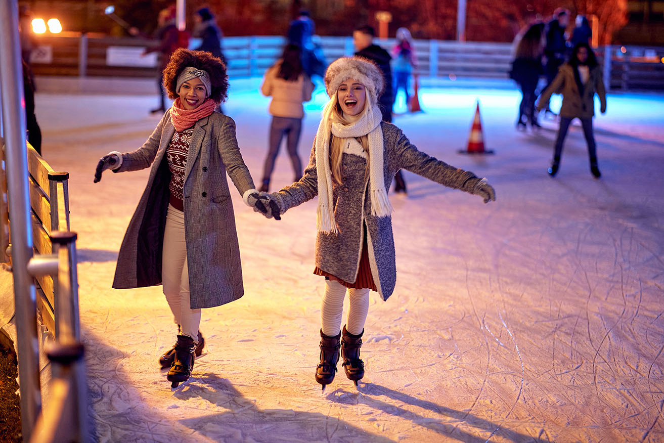 Beautiful gilfriends ice skating together at night; Winter joy concept