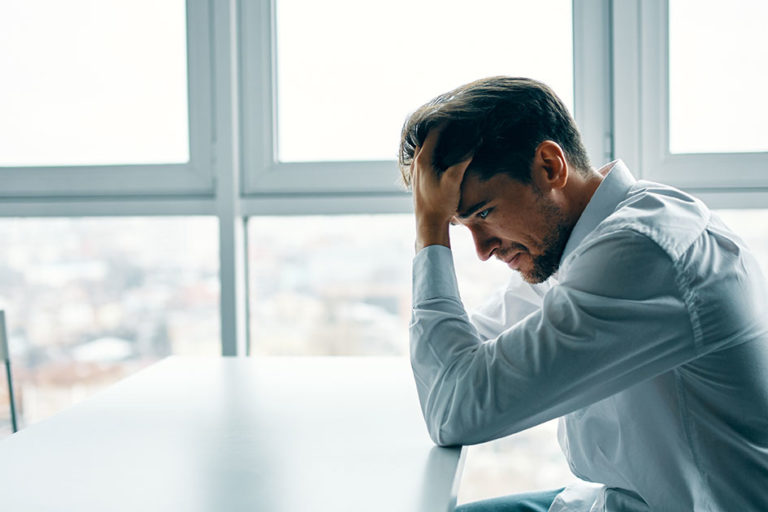 An adult man at the table touches his head with his hand