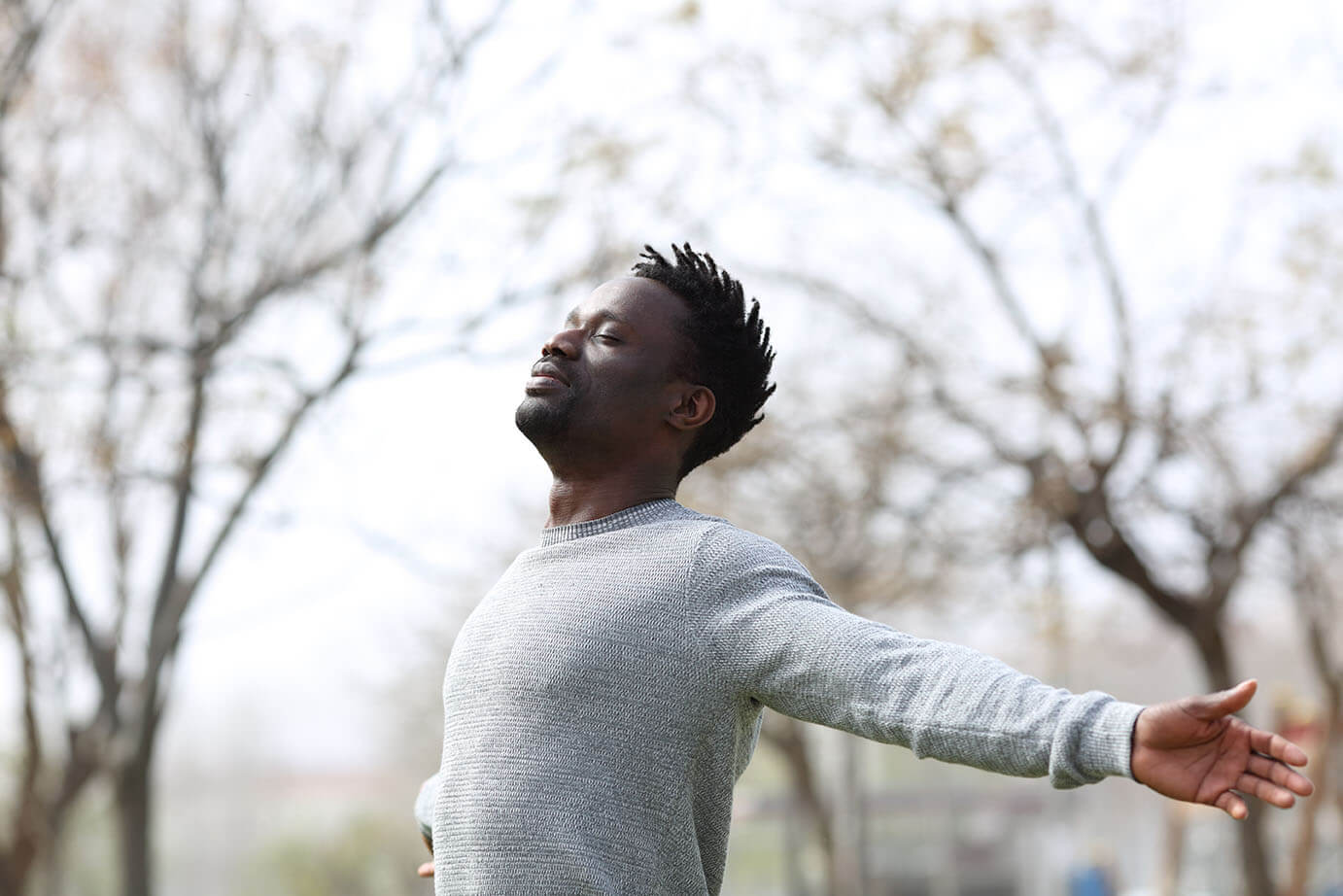 Satisfied black man breathing fresh air with eyes closed standing in the park outdoors