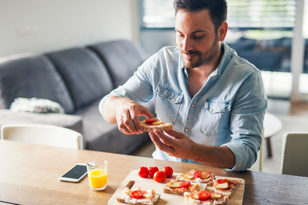 Young modern man eating sandwiches at home